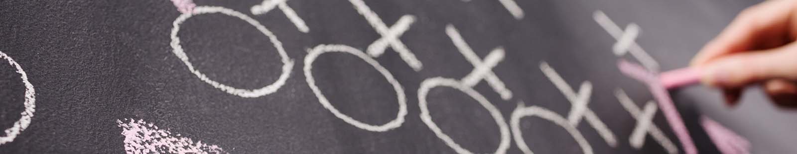 Circles and cross marks being drawn on a chalkboard.
