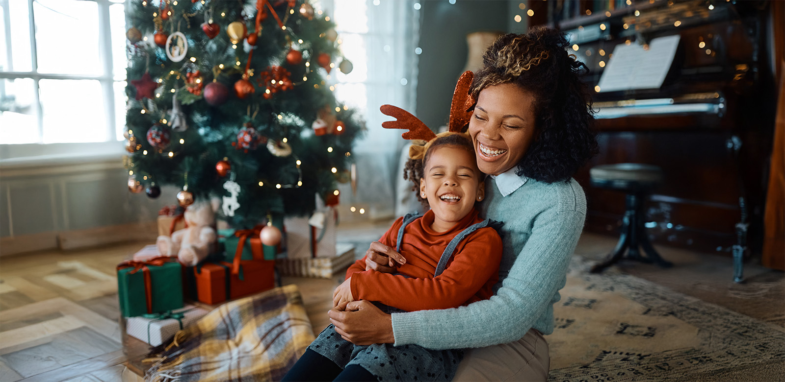 A woman holding her child in front of a Christmas tree.
